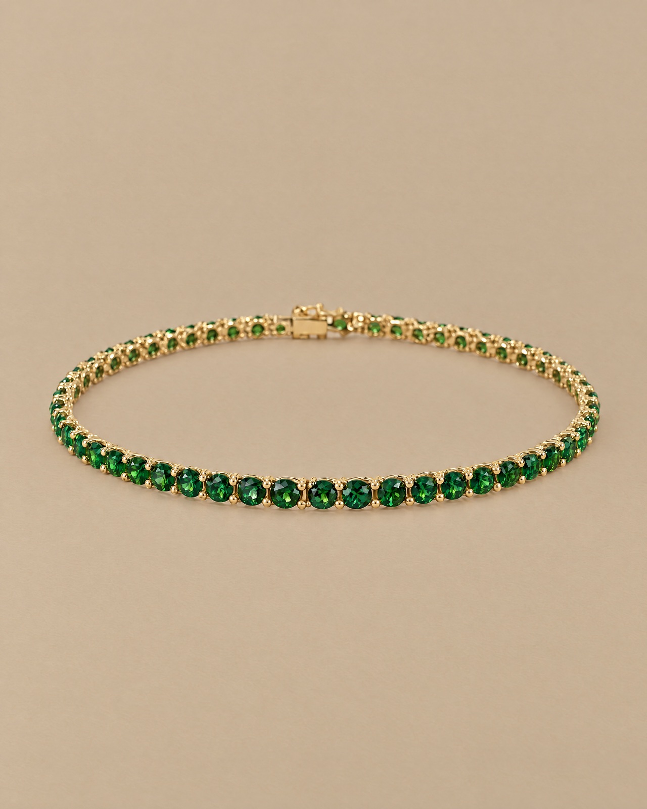 The green tennis bracelet in a still-life photograph on warm beige stone