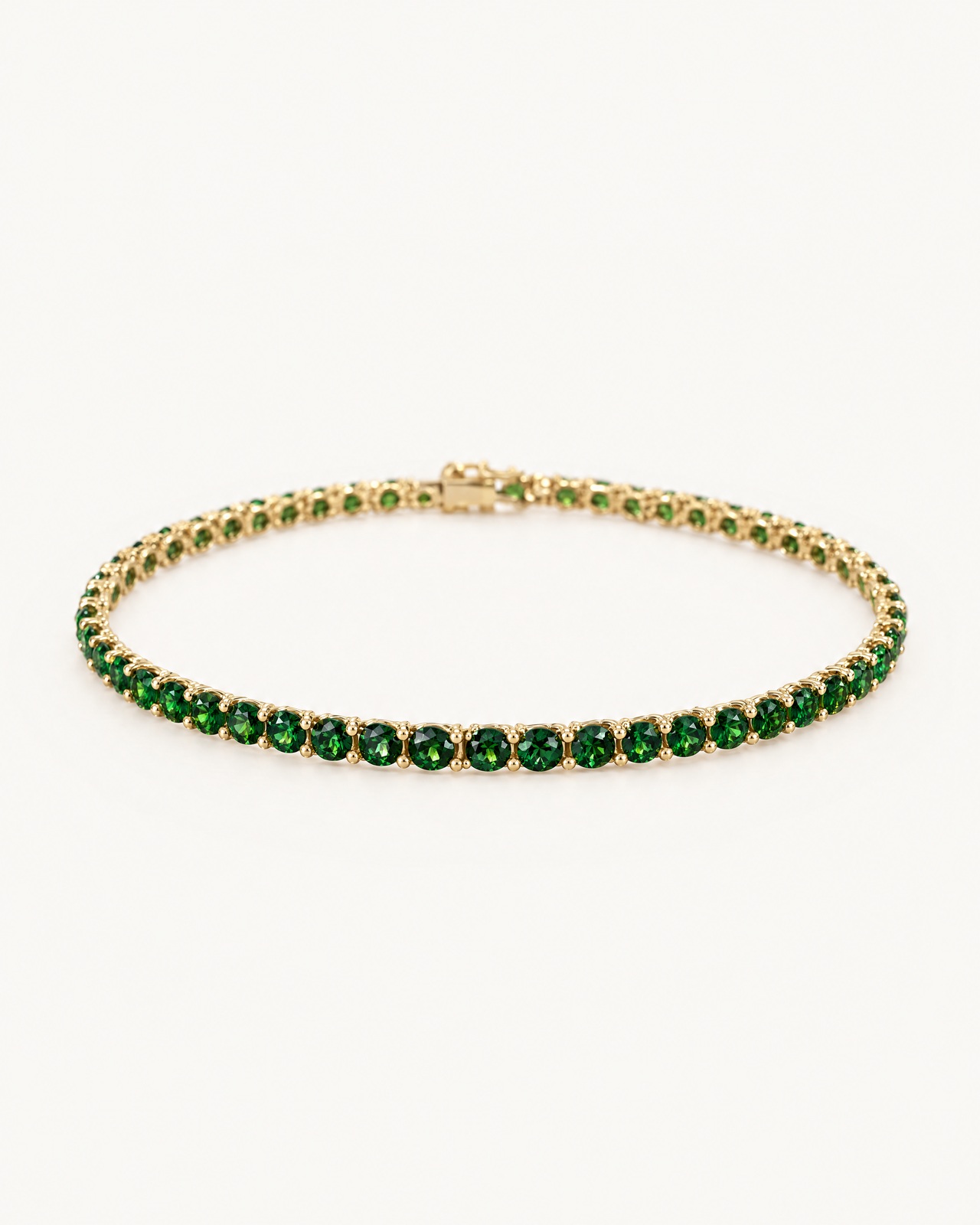 The green tennis bracelet with round green stones in gold-tone prong settings, on an ivory background