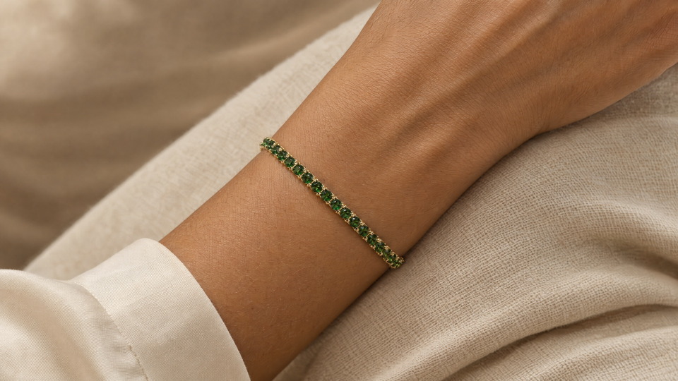 The green tennis bracelet worn on a wrist beside an ivory sleeve