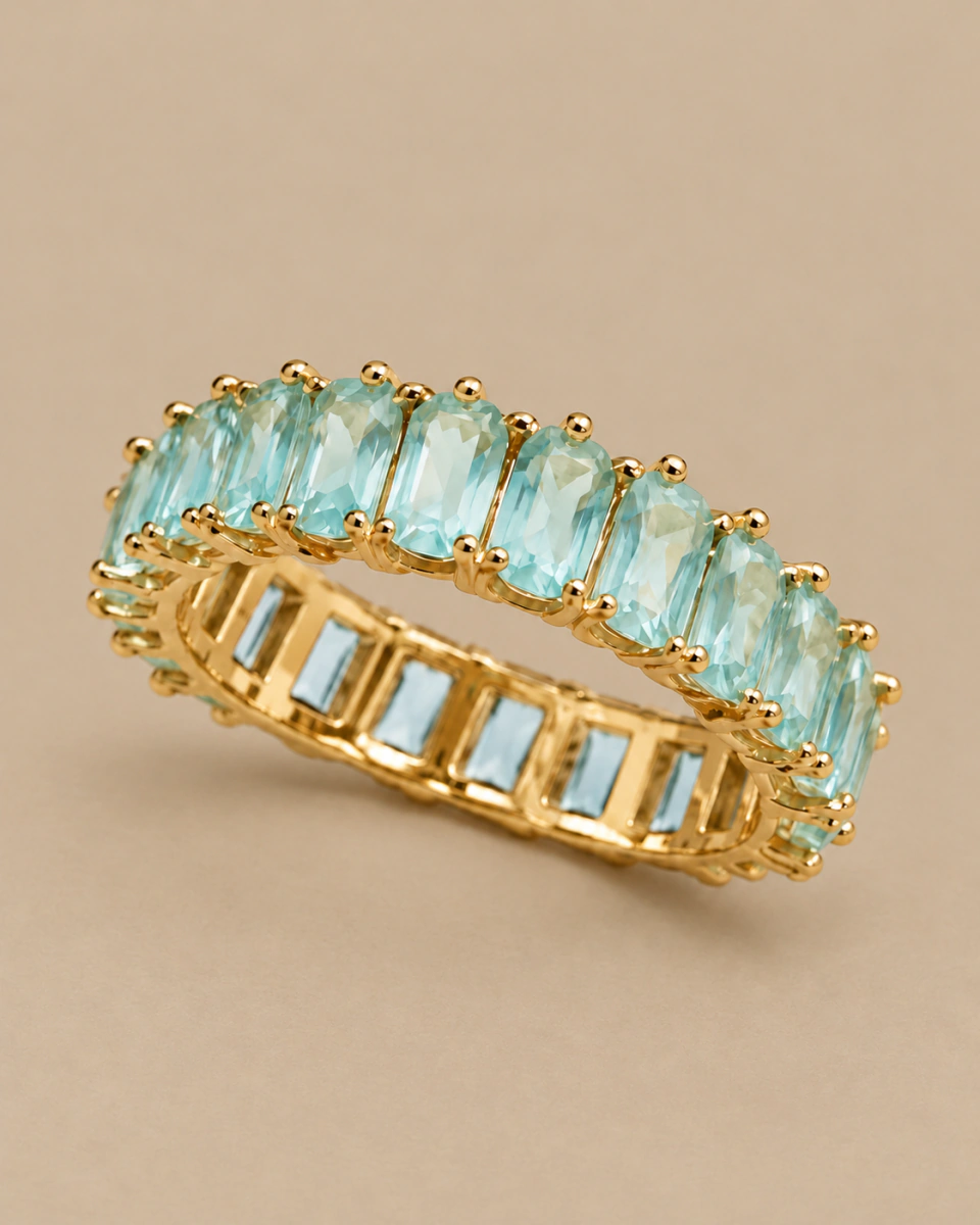 The aqua ring with rectangular stones and an open gold-tone setting, on a warm beige background