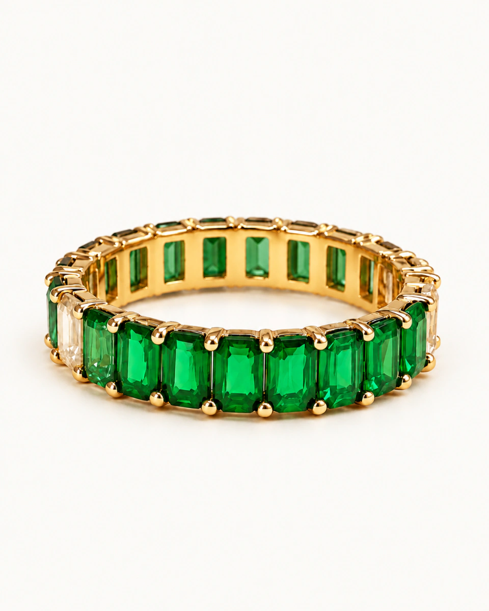 The green ring with rectangular green stones, pale side details and gold-tone prongs, on a light background