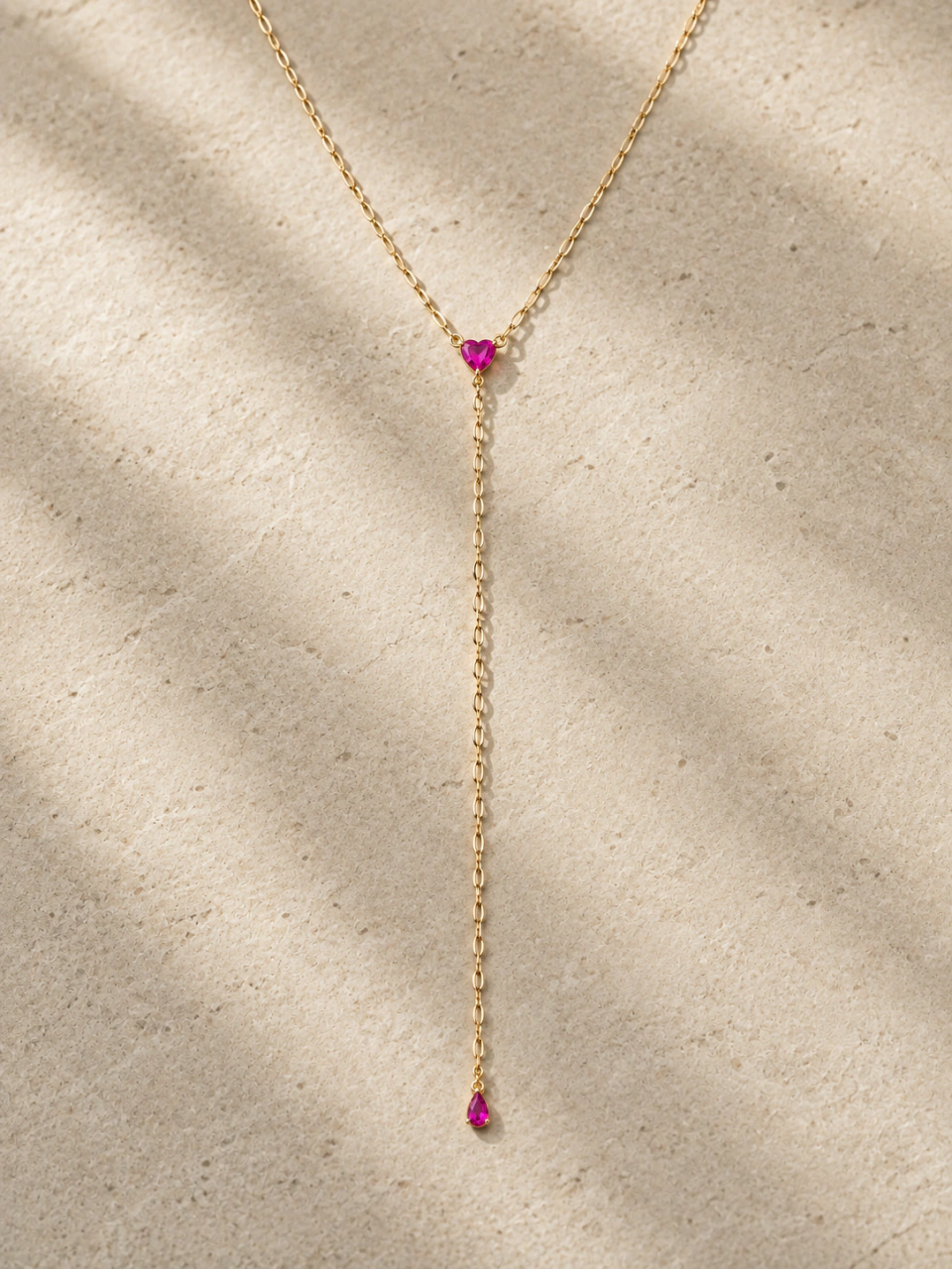 The Roma Necklace (Pink) with its complete chain drop and very tiny pink teardrop terminal, on a warm beige background