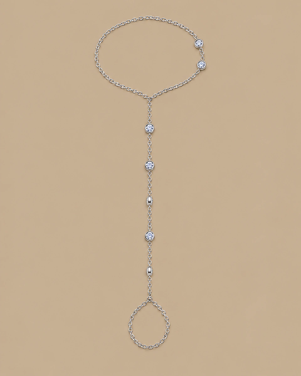 The silver-tone hand chain with its fine connecting chain, on a warm beige background